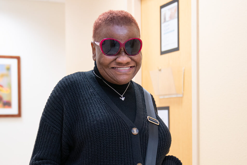 Portrait of a female cancer patient wearing sunglasses, standing in a hallway at the University of Illinois Cancer Center.