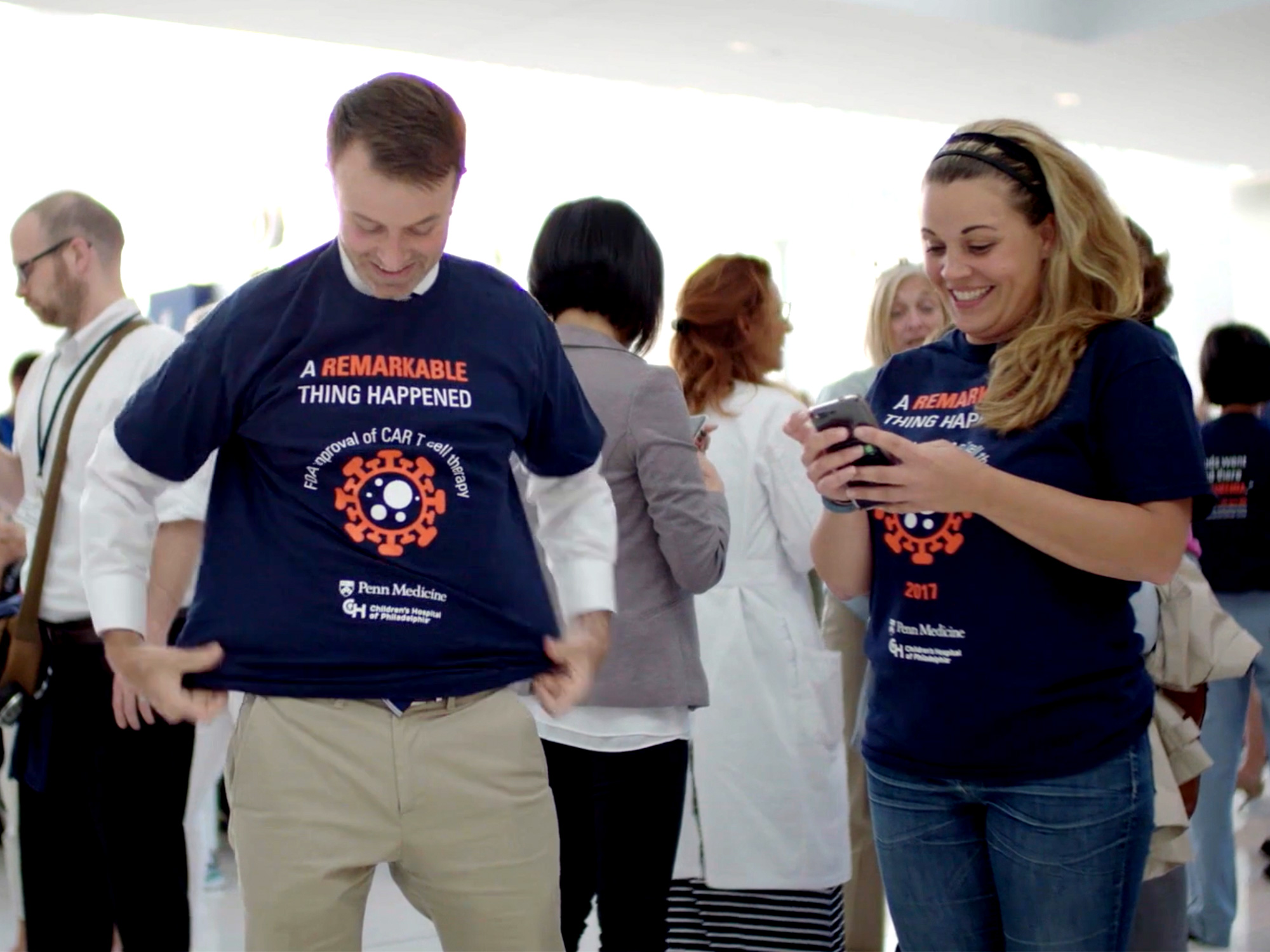 A man and a woman, smiling excitedly, wearing Penn Immunotherapy shirts that read, "A remarkable thing happened: FDA approval of CAR-T cell therapy"